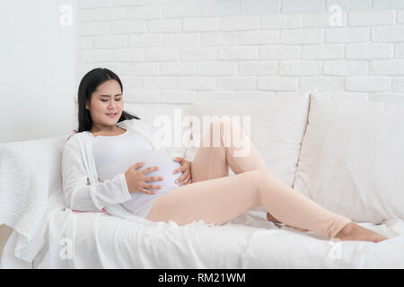 Jungen Asiatischen schwanger sitzen im Wohnzimmer und haben einige wehen. Stockfoto