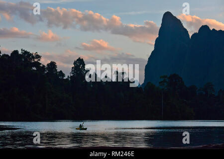 Kajak bei Sonnenaufgang unter KARST Formationen, die sich aus der CHEOW LAN LAKE - Khao Sok Nationalpark, THAILAND Stockfoto