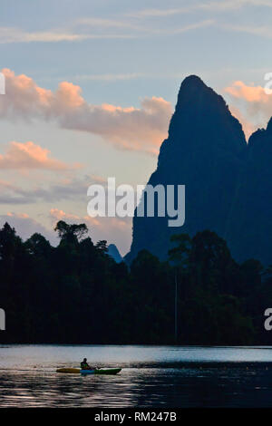 Kajak bei Sonnenaufgang unter KARST Formationen, die sich aus der CHEOW LAN LAKE - Khao Sok Nationalpark, THAILAND Stockfoto