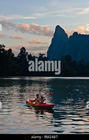 Kajak bei Sonnenaufgang unter KARST Formationen, die sich aus der CHEOW LAN LAKE - Khao Sok Nationalpark, THAILAND Stockfoto