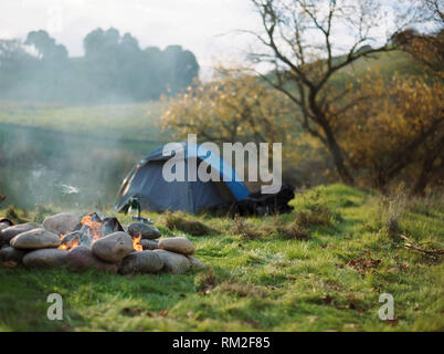 Rauchen Lagerfeuer vor einem Dome Zelt aufgeschlagen auf der Seite von einem Flußufer. Stockfoto