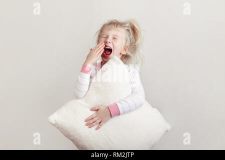 Gesunder Schlaf Konzept. Süße blonde Kaukasische Mädchen in rosa Schlafanzug mit geschlossenen Augen, Gähnen, die weit geöffneten Mund mit Palm. Schläfrige Kind mit m Stockfoto
