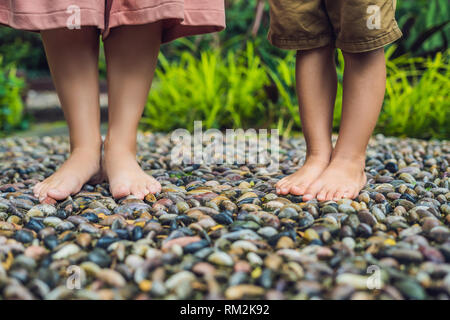 Mutter und Sohn gehen auf eine strukturierte, mit Kopfstein Pflaster, Reflexzonenmassage. Pebble Stones auf dem Bürgersteig für Fußreflexzonenmassage Stockfoto