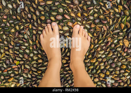 Frau gehen auf eine strukturierte, mit Kopfstein Pflaster, Reflexzonenmassage. Pebble Stones auf dem Bürgersteig für Fußreflexzonenmassage Stockfoto