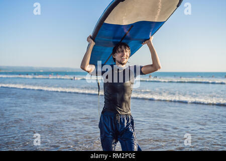 Mann, Surfbrett über seinen Kopf. Nahaufnahme von hübscher Kerl mit Surfbrett auf dem Kopf am Strand. Portrait von Mann Surfboard auf hid Kopf und Stockfoto