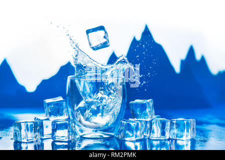 Kristallklares Wasser spritzen in eine doppelte Wand Glas mit Gipfeln im Hintergrund. Eiswürfel in ein Trinkwasser Konzept. Stockfoto