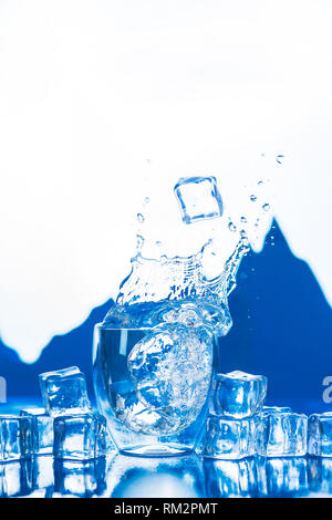 Kristallklares Wasser spritzen in eine doppelte Wand Glas mit Gipfeln im Hintergrund. Eiswürfel in ein Trinkwasser Konzept. Stockfoto