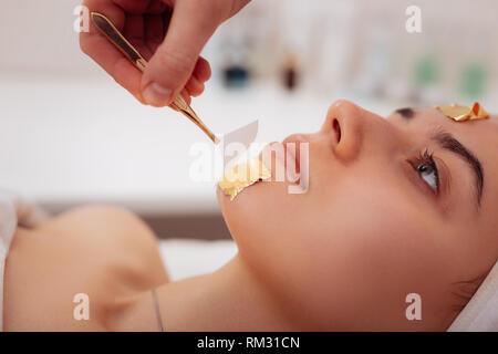 Nahaufnahme von Pinzette entfernen goldene Maske Stockfoto