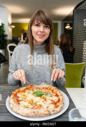 Frau mit Messer und Gabel isst eine Pizza Margherita mit Mozzarella, Tomaten und Basilikum. Neapolitanische Pizza vom Holzofen. Mittagessen in einem Italienischen Stockfoto