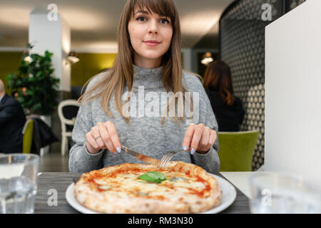 Frau mit Messer und Gabel isst eine Pizza Margherita mit Mozzarella, Tomaten und Basilikum. Neapolitanische Pizza vom Holzofen. Mittagessen in einem Italienischen Stockfoto