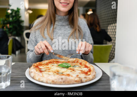 Frau mit Messer und Gabel isst eine Pizza Margherita mit Mozzarella, Tomaten und Basilikum. Neapolitanische Pizza vom Holzofen. Mittagessen in einem Italienischen Stockfoto