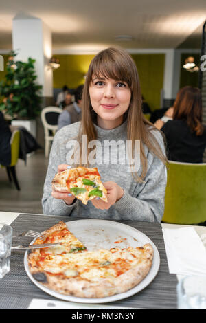 Eine Frau ist Essen neapolitanische Pizza vom Holzofen. Mittagessen in einem italienischen Restaurant. Tisch in der Nähe zu einem großen Fenster. Margarita und vier Käse Stockfoto