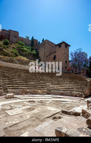 Touristen, die sich in der römischen Amphitheater mit der maurischen Festung oder Alcazaba im Hintergrund, Malaga, Spanien. Stockfoto