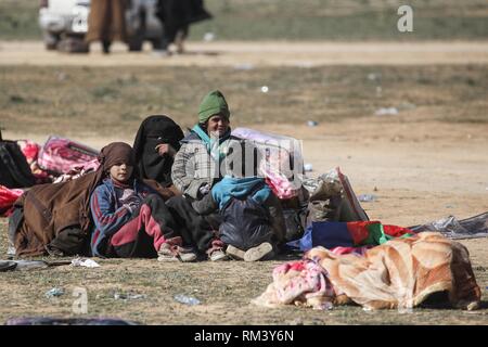 Deir Ezzor, Syrien. 12 Feb, 2019. Eine Familie wartet mit ihrem Gepäck als Zivilisten der islamische Staat fliehen - statt Dorf Baghouz im östlichen syrischen Provinz von Deir Ezzor. Mehr als 1.500 Menschen haben im vergangenen pocket Islamischen Staat im östlichen Syrien in den letzten 48 Stunden Links zu fliehen, die Schlacht zwischen den Kämpfern der syrischen Demokratischen Kräfte (SDF), einer von den USA unterstützten Kurdischen-Gruppe führte, und der Islamischen Staat. Credit: Aboud Hamam/dpa/Alamy leben Nachrichten Stockfoto