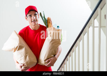 Happy Lieferung Mann in der roten Uniform tragen zwei lebensmittelgeschäfte Säcke aus Papier Stockfoto