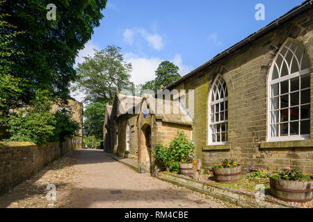 Die Außenseite des lichtdurchfluteten historischen Old School Zimmer, ruhigen Kopfsteinpflasterstraße & Bronte Parsonage Museum darüber hinaus - Church Street, Haworth, West Yorkshire, England, Großbritannien Stockfoto