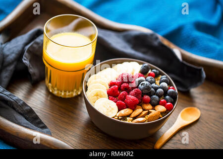 Gesundes Frühstück mit Müsli Schüssel, Beeren, Bananen und Orangensaft in Holz- fach, bed breakfast Stockfoto