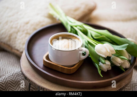 Kaffeetasse mit Tulpen Blumenstrauß in Holzplatte, Haus gemütliche Details im Innenraum, Cappuccino Tasse Stockfoto