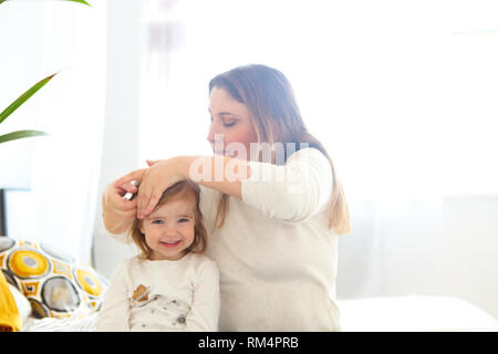 Glücklich liebende Familie. Mutter und Baby Mädchen Spaß machen hairdress sitzen auf dem Bett Stockfoto