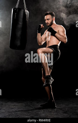 Schöner mann Training in der Nähe von Boxsack auf Schwarz mit Rauch Stockfoto