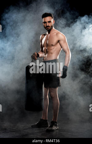 Muskulöse boxer Holding Boxsack auf Schwarz mit Rauch Stockfoto