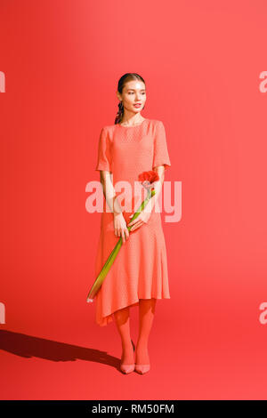 Attraktive elegante Mädchen im Kleid mit roten Amaryllis, Blume auf lebende Koralle. Pantone-Farbe des Jahres 2019 Konzept Stockfoto