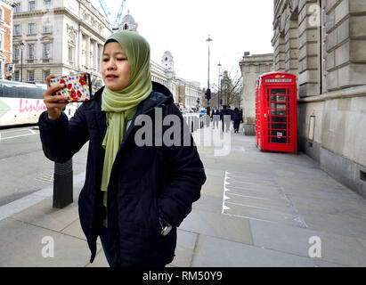 London, England, UK. Asiatische Frau am Handy - traditionelle rote Telefonzelle im Hintergrund - Whitehall Stockfoto