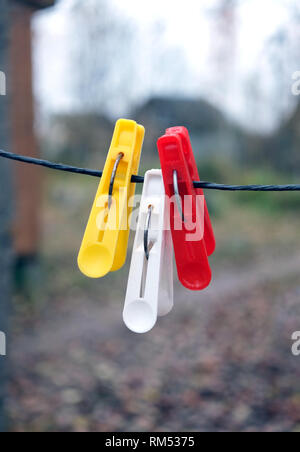 Drei farbigen Wäscheklammern hängen schwarz Seil auf einer unscharfen Hintergrund im Herbst Tag im Freien vertikale Ansicht Nahaufnahme Stockfoto