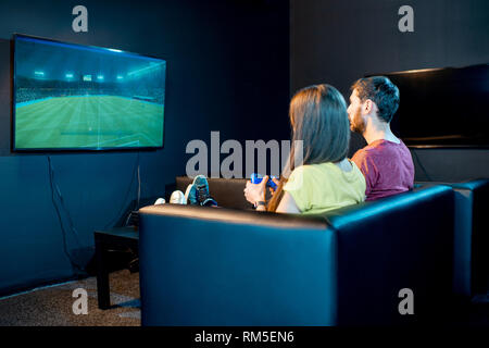 Junges Paar Fußball spielen Spiel mit Spielkonsole sitzen auf der Couch am Spielen Club, Rückseite mit TV-Bildschirm Stockfoto