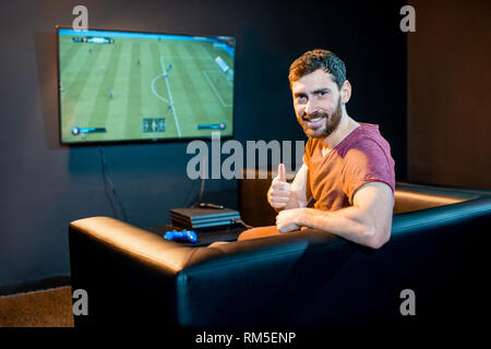 Portrait eines glücklichen Menschen mit Joy stick spielen Fußball Spiel mit Spielkonsole sitzen auf der Couch am Spielen Club Stockfoto