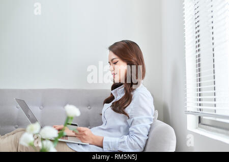 Eine schöne mit Laptop und Ihre Kreditkarte beim Einkaufen von zu Hause aus ohne Wohnzimmer Sofa Stockfoto