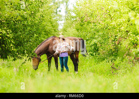 Aktive Frau in westlichen Cowgirl Hut wandern mit Pferd. American Girl in der Landschaft Ranch. Stockfoto