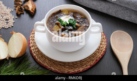 Traditionelle Pilzsuppe von Pilzen. Holzlöffel, Dill und Zwiebeln auf dem Tisch Stockfoto
