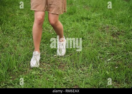 Mädchen Spaziergänge auf dem Gras. Frau in weißen Turnschuhen und Kleid läuft auf grünem Gras Stockfoto