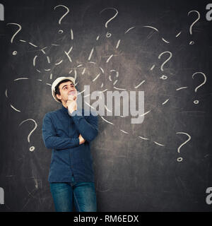 Positive junge Mann Ingenieur das Tragen schützender helm die Hand unter dem Kinn bis nachdenklich auf der Suche vor einer Tafel versuchen verschiedene zu lösen Stockfoto