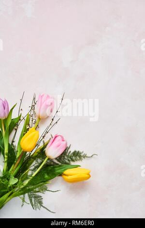 Rosa und gelbe Tulpen Blumen auf rosa Hintergrund. Ansicht von oben mit der Kopie Platz für Text. Warten auf Frühling. Frohe Ostern Karte. Flach. Feder Konzept. Stockfoto