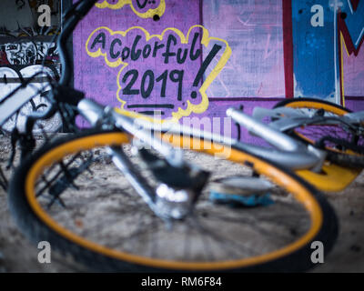 Alte gelbe Schrott, Fahrräder unter Beton Treppe mit violett Graffiti Hintergrund und Tag des neuen Jahres für eine bunte 2019 Stockfoto