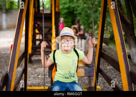 Blonde Junge mit Hut und Brille mit speziellen Linse auf dem Spielplatz. Stockfoto