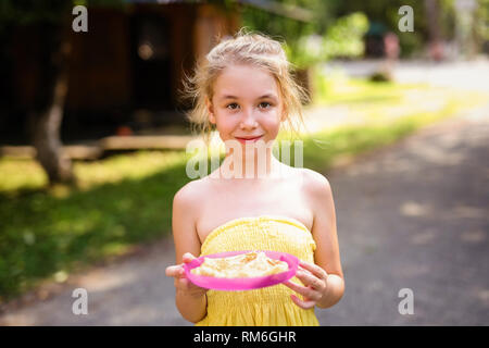 Blond lächelnde Mädchen mit Platte Pfannkuchen im Land. Stockfoto
