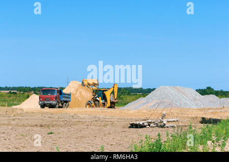Bagger- und Lkw-Arbeiten auf der Baustelle, Baumaschinen und einen Haufen Sand Stockfoto