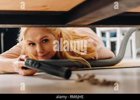 Lächelnde ältere Frau mit Staubsauger unter Möbeln Stockfoto