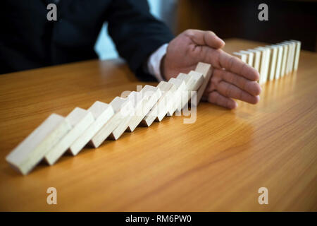 Geschäftsmann Hand hält Domino kontinuierliche umgeworfen, was bedeutet, dass das Scheitern von Unternehmen behindert. Stop über dieses Geschäft Ausfallkonzept. Stockfoto