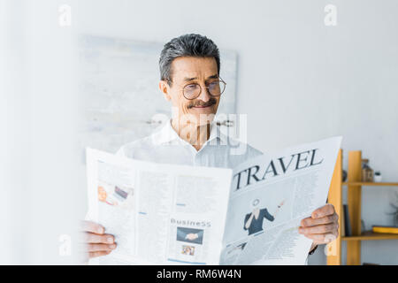 Fröhlicher älterer Mann lesen Reisen Zeitung zu Hause Stockfoto