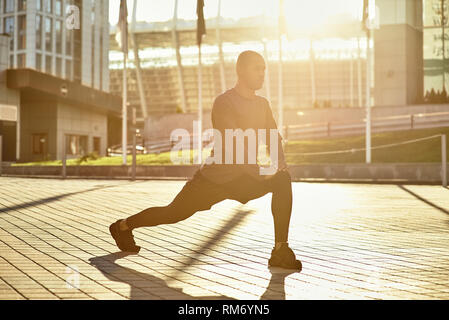 Stretching nach dem Großen Workout. Seitenansicht des Athleten stretching Beine während der morgendlichen Workout Am sonnigen Tag. Gesunde Lebensweise. Sport motivation Konzept. Fitness Concept. Stockfoto