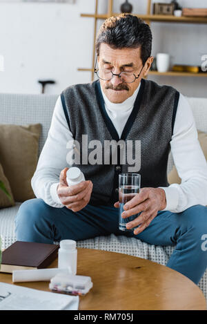 Älterer Mann an der Flasche mit Pillen halten Glas Wasser Stockfoto