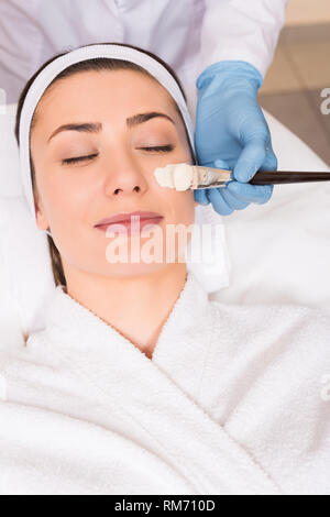 Beginn Kosmetikerin kosmetische Maske auf Frau Gesicht mit Kosmetik Pinsel an Beauty Salon anzuwenden Stockfoto