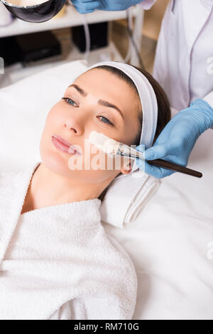 Beginn Kosmetikerin kosmetische Maske mit Kosmetik Pinsel auf Frau Gesicht im Beauty Salon anzuwenden Stockfoto