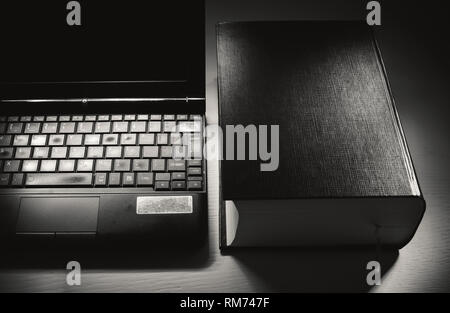 Konzeptionelle Zusammensetzung über Wissen, alte geöffnet Laptop und Buch. Stockfoto