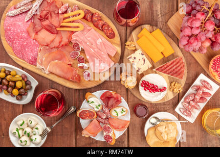 Gourmet Wurstwaren. Eine Auswahl an Wurst und Schinken, Aufschnitt, und eine Käseplatte, geschossen von oben auf einem dunklen Hintergrund im Landhausstil mit Wein Stockfoto