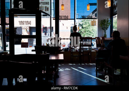 In diner Harlem in New York City. Kunden sitzen mit Kaffee und Laptop gegen die helle Straße und Sonnenschein Silhouette Stockfoto
